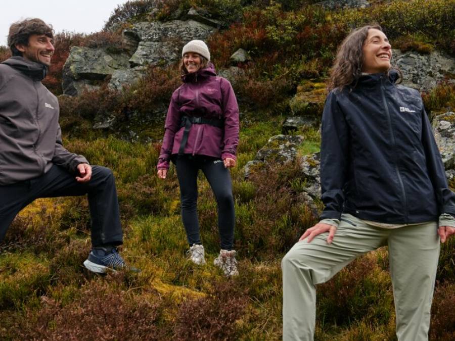 Three smiling friends standing on rocky terrain and observing the landscape