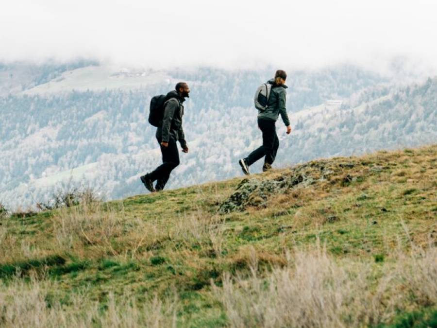 Four people in summer hiking gear run across a field